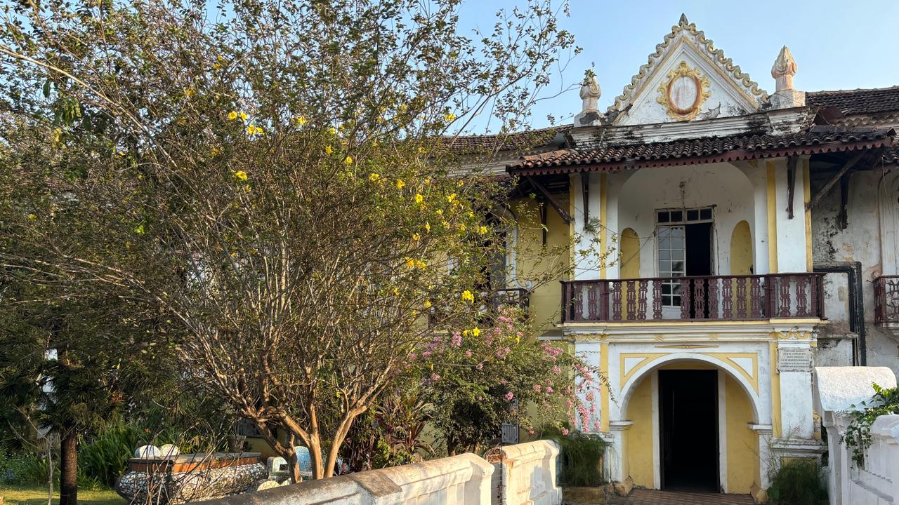 Exterior view of Braganza House in Chandor, Goa, showcasing its grand colonial architecture with large windows, ornate balconies, and lush greenery surrounding the estate.